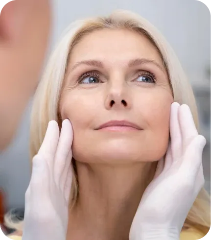 Mulher madura em avaliação facial, com as mãos do profissional delimitando o contorno do rosto